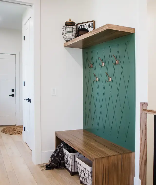 Custom entryway bench with wood top, built-in storage, and a decorative green wall panel with hooks, showcasing detailed millwork by Hiebert Cabinets.
