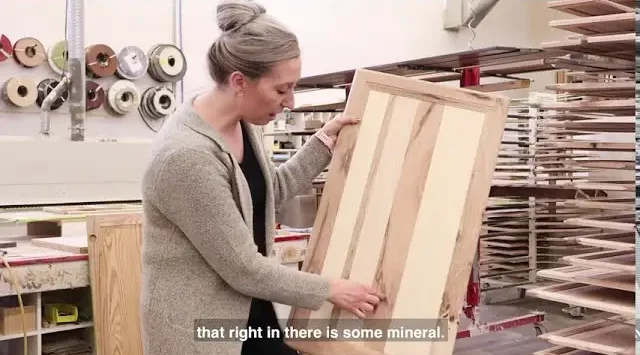 Craftsperson examining a custom cabinet panel in the workshop, highlighting natural wood grain variations and fine woodworking by Hiebert Cabinets.