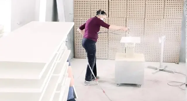 Craftsperson spray-finishing custom cabinet panels in a professional woodworking shop, highlighting Hiebert Cabinets’ high-quality finishing process.