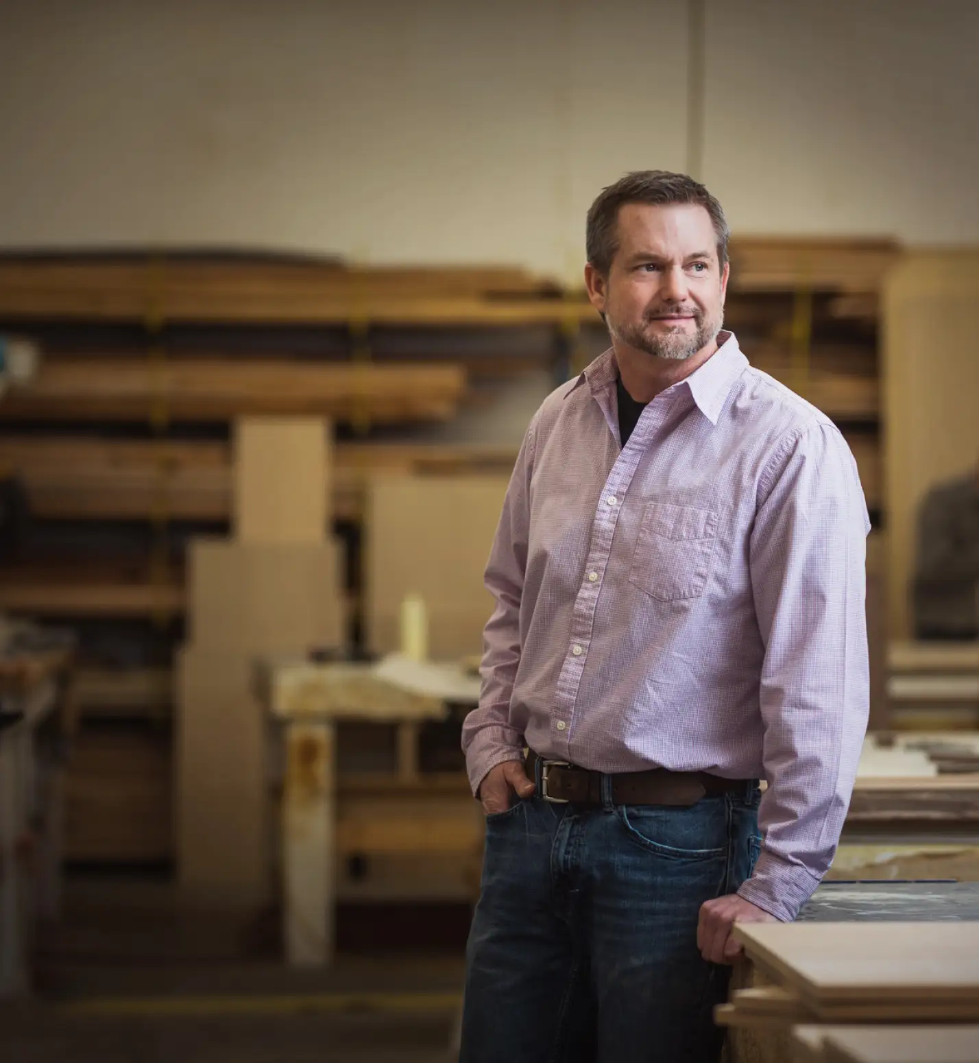 Cabinetry craftsman standing in a custom woodshop surrounded by lumber and workbenches, representing the expertise behind Hiebert Cabinets’ custom woodworking.
