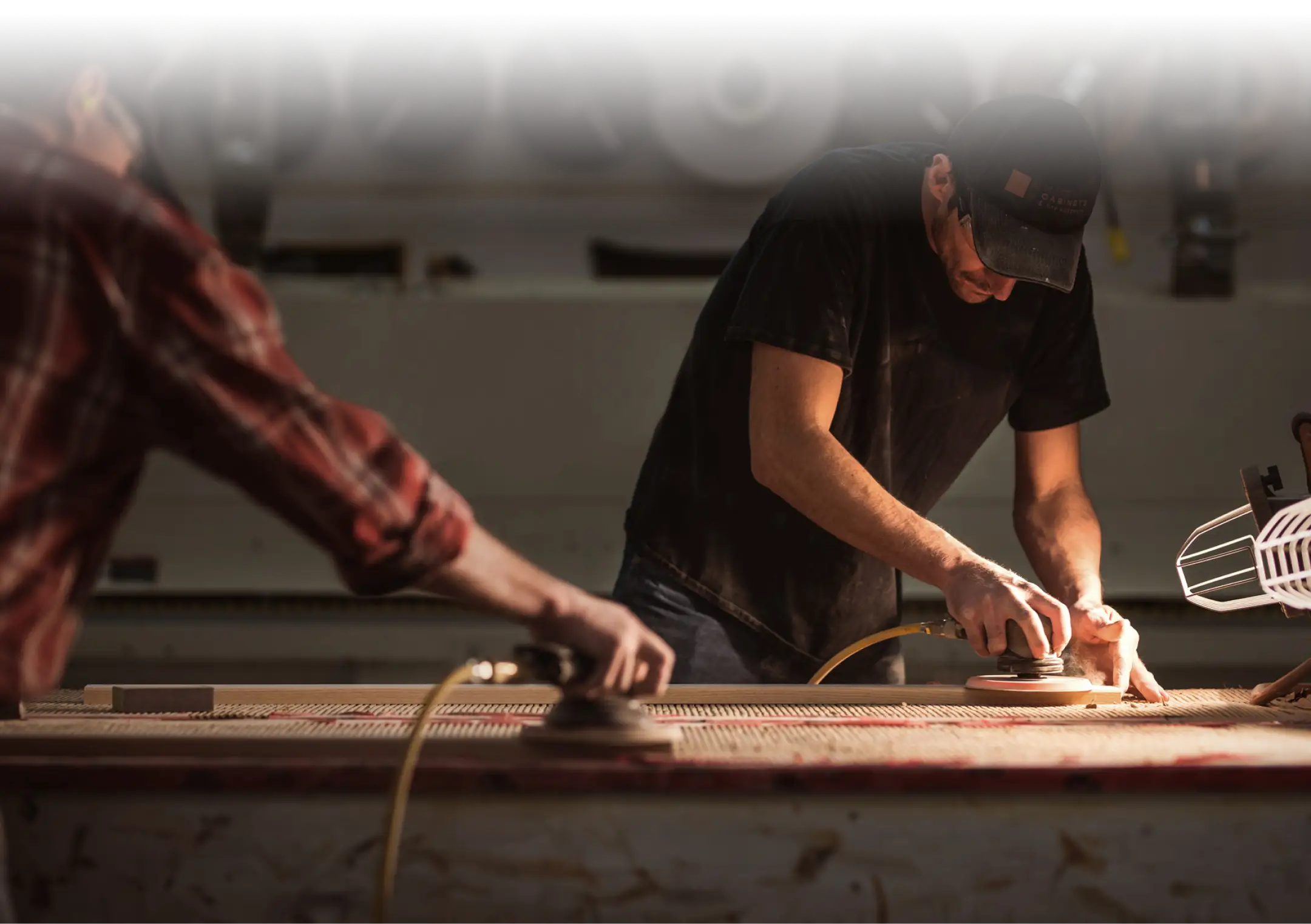 Woodworkers sanding custom cabinetry components in the shop, highlighting skilled craftsmanship and detailed finishing work.