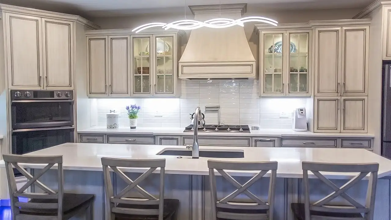 Elegant kitchen featuring custom cream-finished cabinets with glass fronts, detailed range hood millwork, and a large island with handcrafted cabinetry by Hiebert Cabinets.