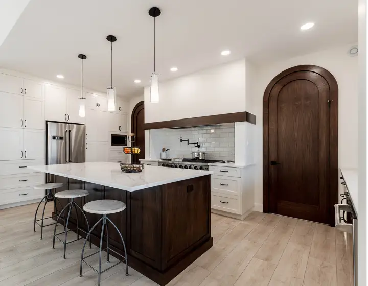 Modern kitchen featuring a dark wood custom island, white shaker cabinets, arched wood doors, and detailed millwork crafted by Hiebert Cabinets.