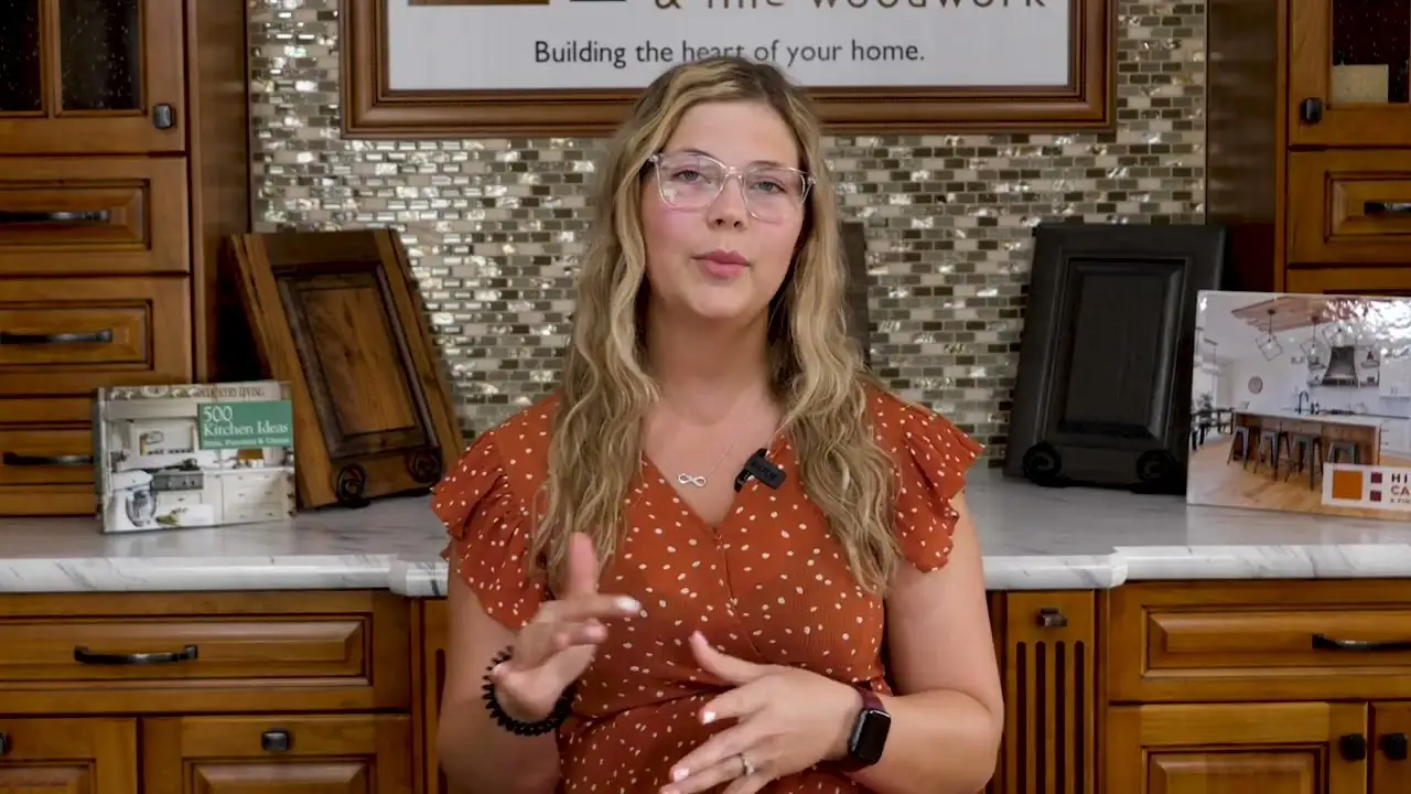 Woman explaining custom cabinets in a showroom with detailed wood cabinet doors and handcrafted woodwork samples displayed on the counter.