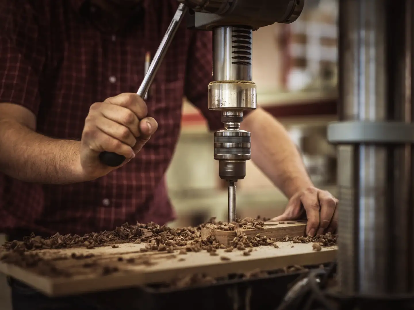 Craftsman drilling into hardwood while shaping custom cabinetry components with precision woodworking techniques.