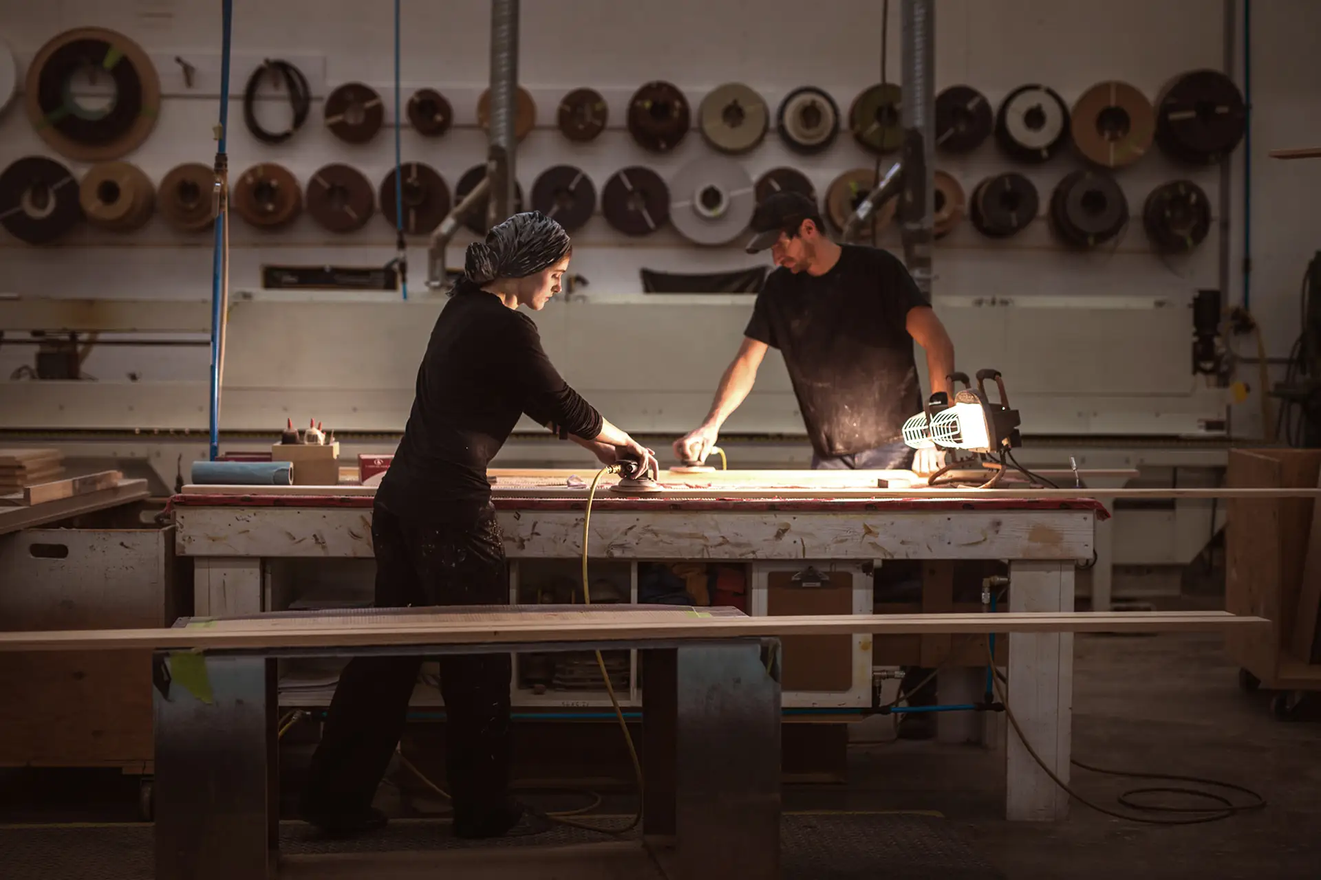 Two woodworkers sanding and preparing custom cabinetry components in a professional workshop, surrounded by tools and finishing materials.