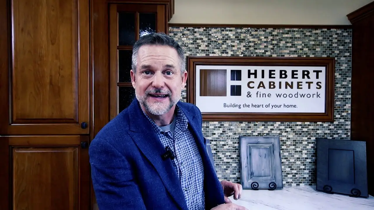 Representative standing in front of custom wood cabinetry and a Hiebert Cabinets sign, showcasing fine woodwork and handcrafted cabinet design.