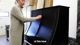 Craftsperson inspecting a custom-built black cabinet with curved panel fronts inside the Hiebert Cabinets workshop.