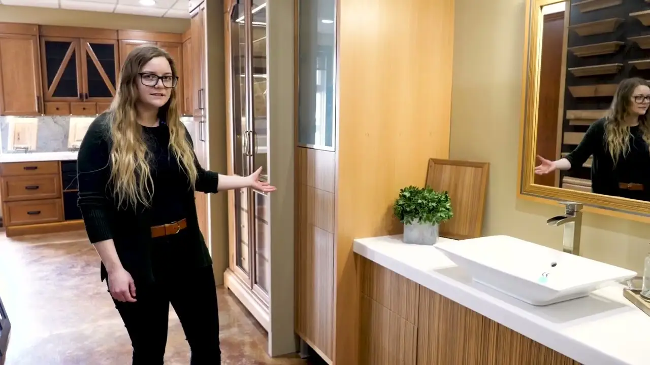Custom kitchen cabinets with a pull-out utensil organizer displayed by a designer, showcasing detailed woodwork, soft-close drawers, and various cabinet door samples in a showroom.