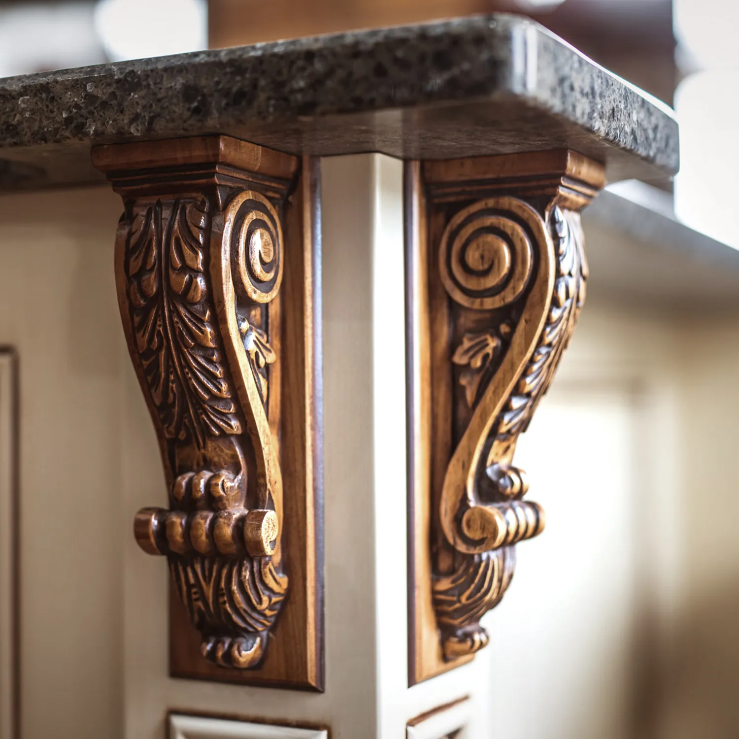 Close-up of custom carved wood corbels supporting a granite countertop, showcasing detailed scrollwork and fine craftsmanship in luxury kitchen cabinetry.