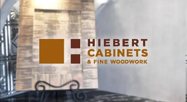 Hiebert Cabinets & Fine Woodwork logo displayed in a showroom setting with custom wood panels and handcrafted millwork.